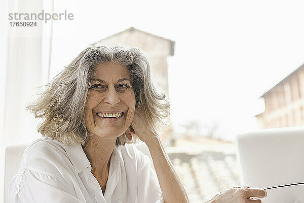 Happy senior woman sitting in front of window at home