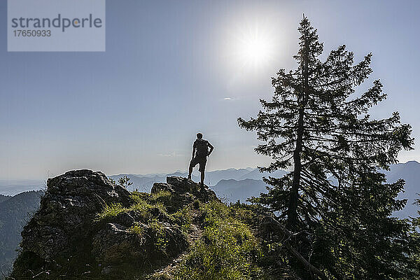 Deutschland  Bayern  Sonne scheint über der Silhouette eines männlichen Wanderers  der allein auf dem Berggipfel steht