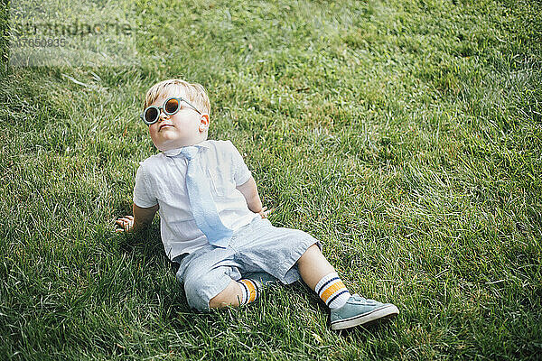 Junge mit Sonnenbrille und Krawatte sitzt auf Gras