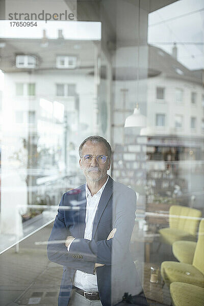 Geschäftsmann mit verschränkten Armen durch Glasfenster im Café gesehen