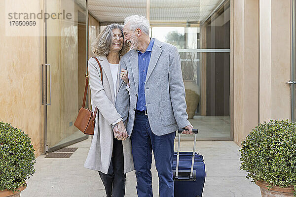 Fröhliches älteres Paar mit Koffer bei der Ankunft im Boutique-Hotel