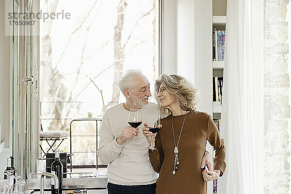 Glückliches älteres Paar mit Weingläsern  das in der Hotelwohnung steht