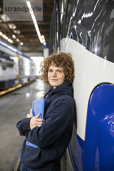 Lächelnder Ingenieur hält Aktenordner in der Hand und stützt sich auf die Einschienenbahn in der Industrie