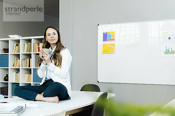 Businesswoman holding coffee cup sitting on desk in office