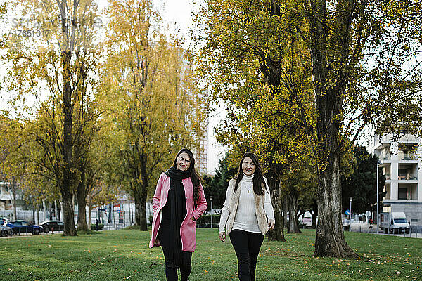 Glückliche Schwestern  die vor Bäumen im öffentlichen Park spazieren