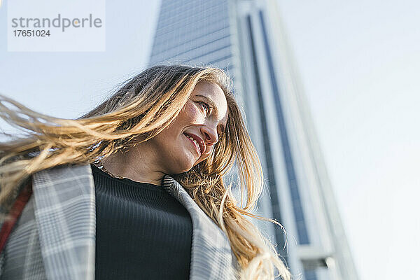 Lächelnde Frau  die an einem sonnigen Tag vor dem Gebäude steht