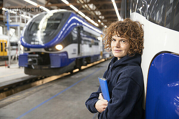 Selbstbewusster Ingenieur hält Aktenordner in der Hand und stützt sich auf die Einschienenbahn in der Industrie