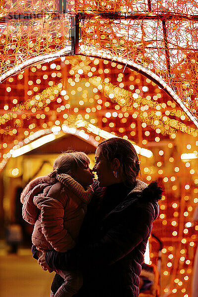 Mother embracing daughter standing by Christmas lights