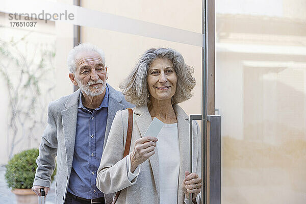 Älteres Paar mit Schlüsselkarte steht an der Glastür eines Boutique-Hotels