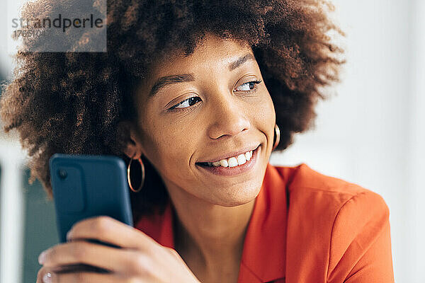 Lächelnde Geschäftsfrau mit Afro-Frisur hält Mobiltelefon in der Hand