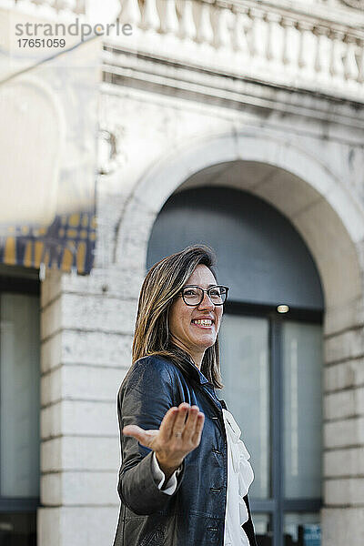 Lächelnde Frau gestikuliert stehend in der Stadt