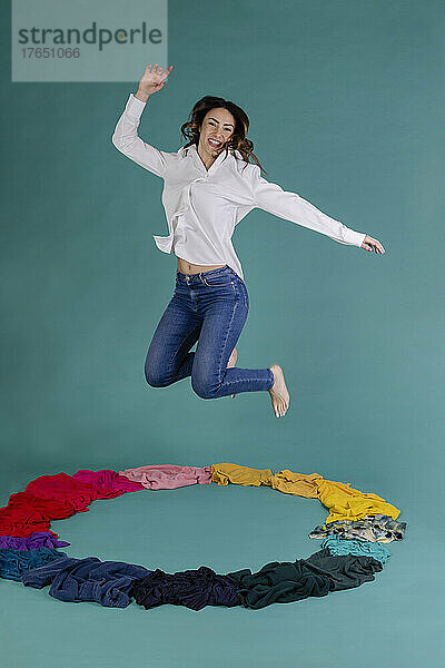 Happy woman jumping over clothes against blue background