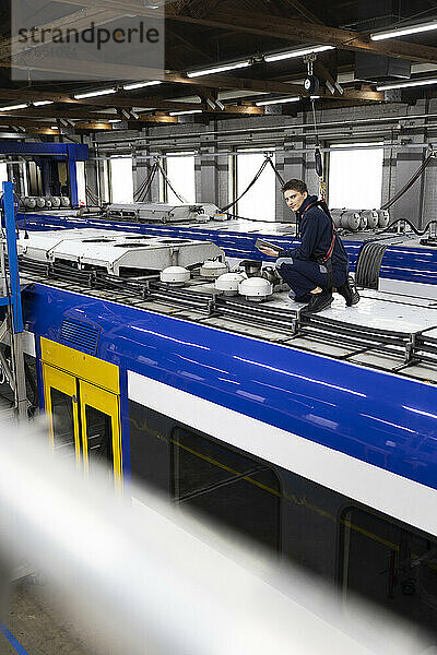 Ingenieur hält Tablet-PC in der Hand und sitzt auf dem Dach einer Einschienenbahn in der Industrie