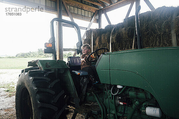 Glücklicher Junge sitzt auf dem Fahrersitz des Traktors im Bauernhof
