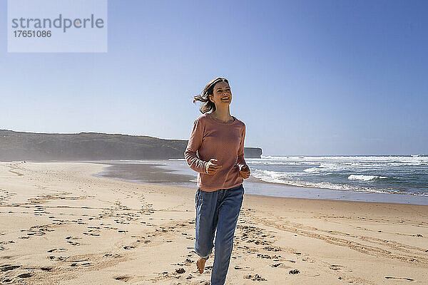 Glückliche Frau läuft an einem sonnigen Tag am Strand