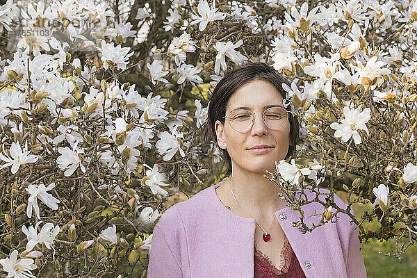 Lächelnde Frau mit geschlossenen Augen steht inmitten blühender Magnolienbäume