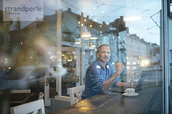 Freiberufler mit Laptop durch Glasfenster im Café gesehen