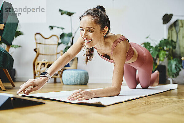 Glückliche Frau berührt Tablet-PC auf der Trainingsmatte zu Hause