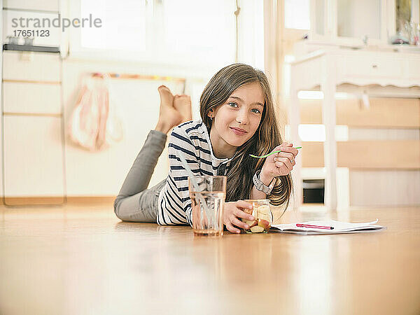 Lächelndes Mädchen  das zu Hause auf dem Boden liegend Obstsalat isst