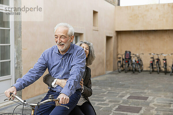 Ältere Frau sitzt mit Mann auf Fahrrad vor Gebäude