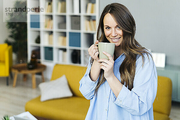 Lächelnde junge Frau mit Kaffeetasse zu Hause