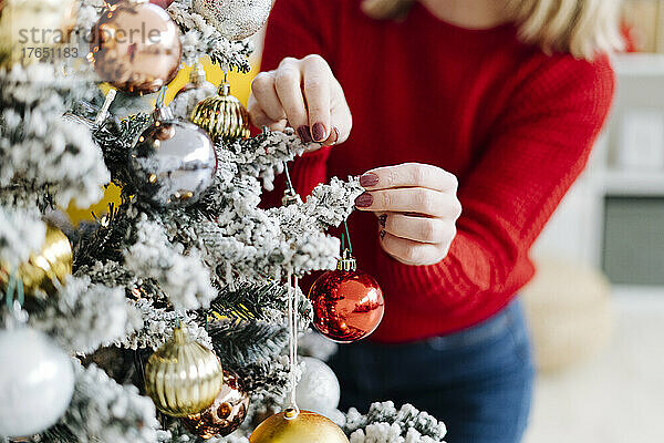 Frau schmückt zu Hause den Weihnachtsbaum mit Christbaumkugel