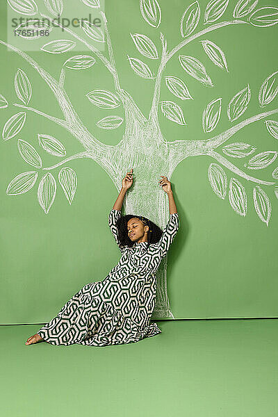 Junge Frau mit geschlossenen Augen stützt sich auf einen Baum und zeichnet vor grünem Hintergrund