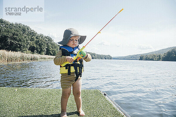 Niedlicher kleiner Junge mit Angelrute steht an einem sonnigen Tag am Fluss