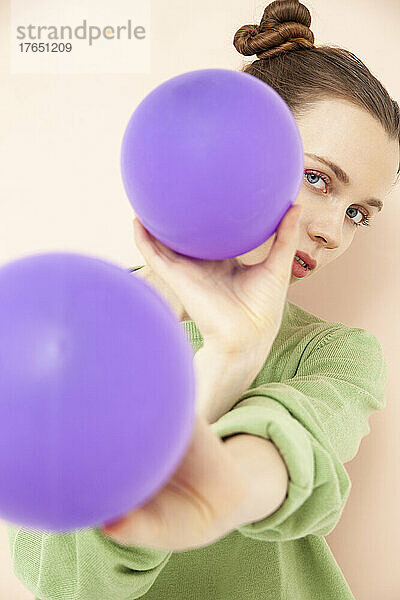 Beautiful woman with purple balloons against peach background