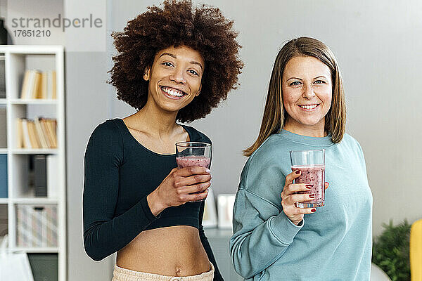 Glückliche Frauen mit Gläsern Smoothie  die zu Hause im Wohnzimmer stehen