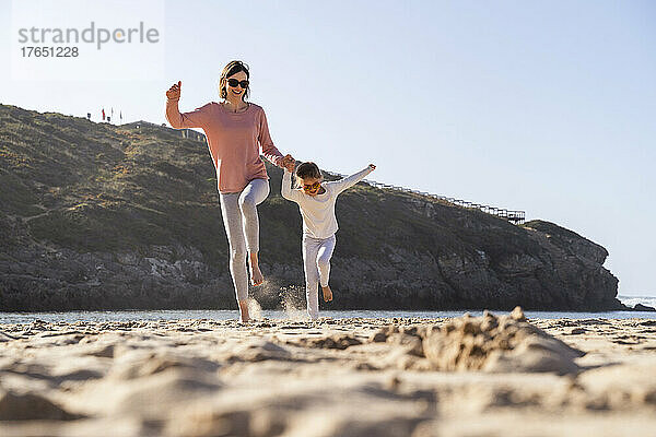 Glückliche Mutter und Tochter springen am Strand auf Sand