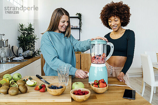 Glückliche junge Frau steht neben einem Freund und bereitet Smoothie in der Küche zu