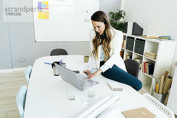 Lächelnde Geschäftsfrau benutzt Laptop am Schreibtisch im Büro