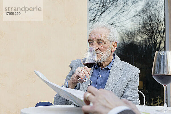 Älterer Mann trinkt Wein und sitzt am Tisch