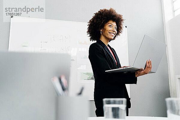 Lächelnde Geschäftsfrau mit Laptop vor dem Whiteboard