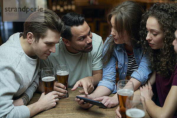 Gruppe von Freunden  die in einer Kneipe Bier trinken und ein Smartphone teilen