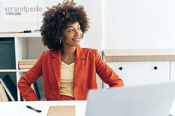 Lächelnde Geschäftsfrau mit Laptop sitzt am Schreibtisch im Büro
