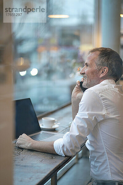 Geschäftsmann schaut durchs Fenster und telefoniert im Café