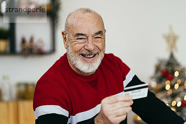 Glücklicher älterer Mann  der zu Hause eine Kreditkarte hält