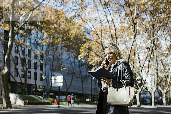 Frau spricht mit Smartphone und liest Tagebuch in der Stadt