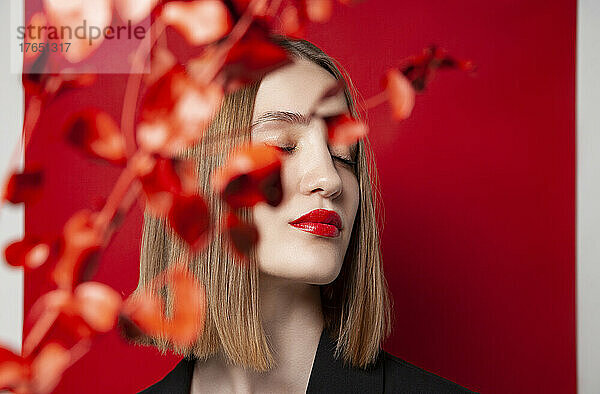Schöne blonde Frau mit geschlossenen Augen hinter einem Zweig vor rotem Hintergrund