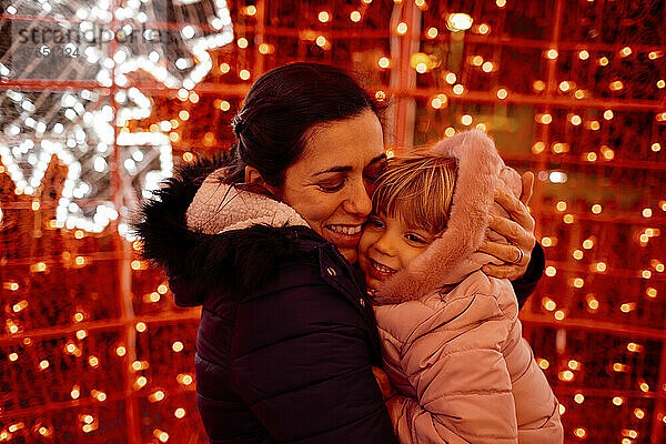 Glückliche Mutter umarmt Tochter vor Weihnachtsbeleuchtung