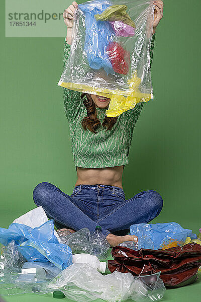 Lächelnde Frau entfernt Plastikmüll vor grünem Hintergrund
