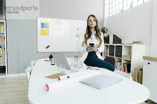Geschäftsfrau mit Smartphone sitzt am Schreibtisch im Büro