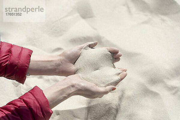 Hände einer Frau mit Sand an einem sonnigen Tag