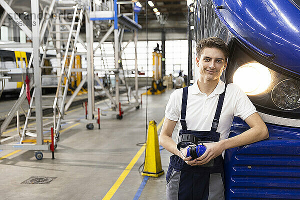 Smiling young trainee standing by monorail in factory