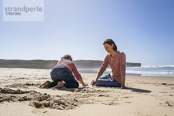 Mutter und Tochter schreiben auf Sand am Strand