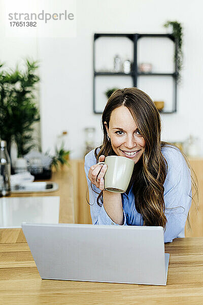 Lächelnder Freiberufler mit Laptop und Kaffeetasse zu Hause