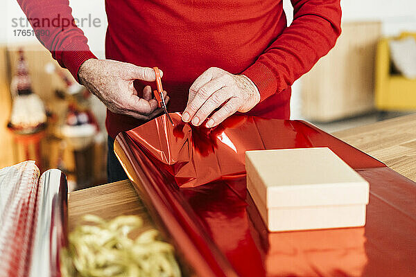 Hand eines älteren Mannes  der zu Hause Weihnachtsgeschenk auf den Tisch packt