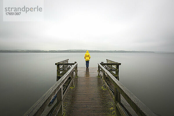 Deutschland  Schleswig-Holstein  Frau in gelber Jacke steht am Rand eines Stegs am Seeufer